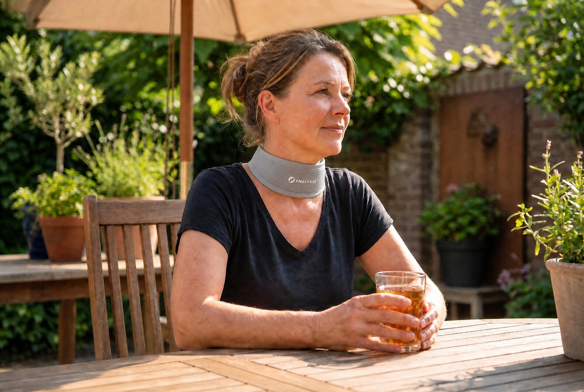 Vrouw met nekkoeler aan een tafel in een zonnige tuin